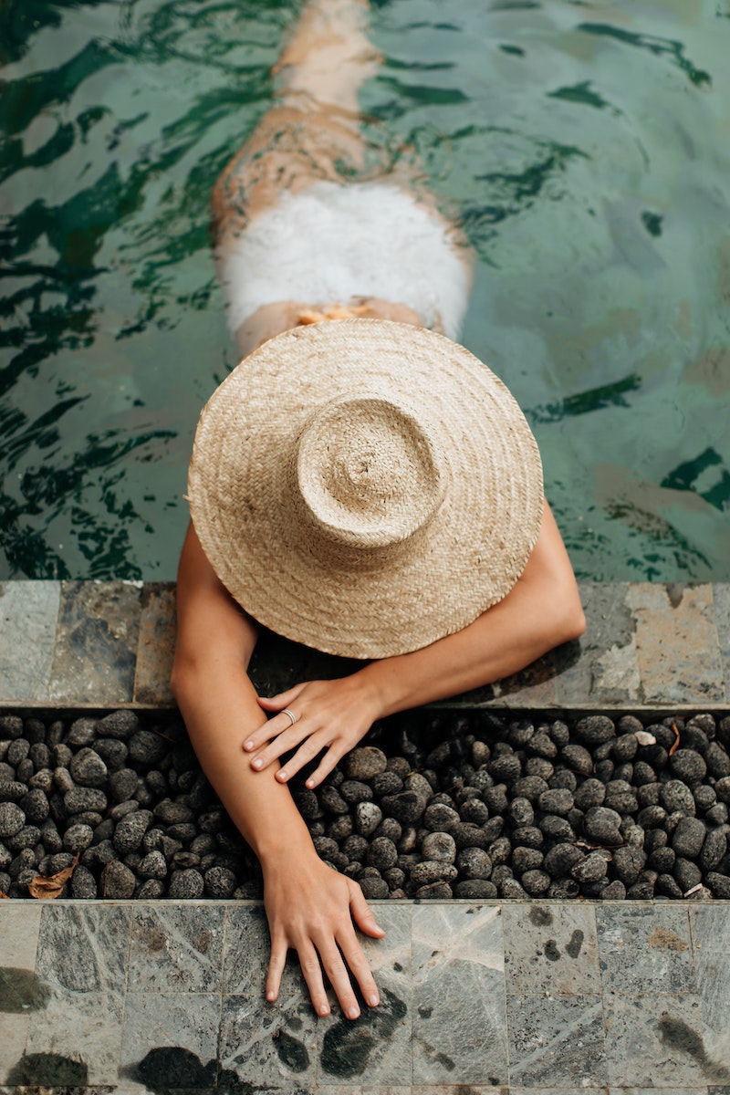 woman swimming in pool with wide brim straw hat
